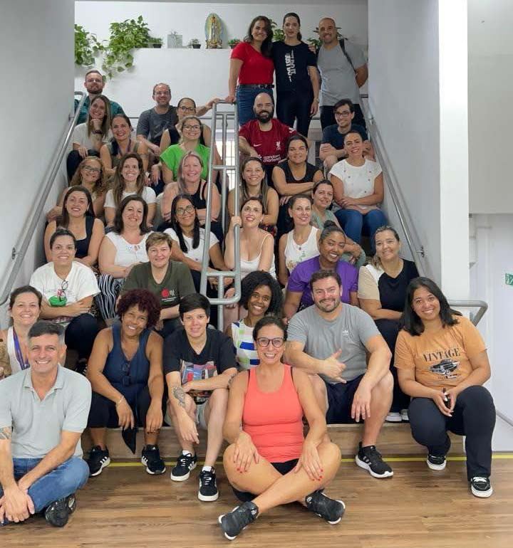 Equipe de professores e colaboradores do Colégio Reggio Emilia reunida, sorrindo, em uma escadaria interna da escola