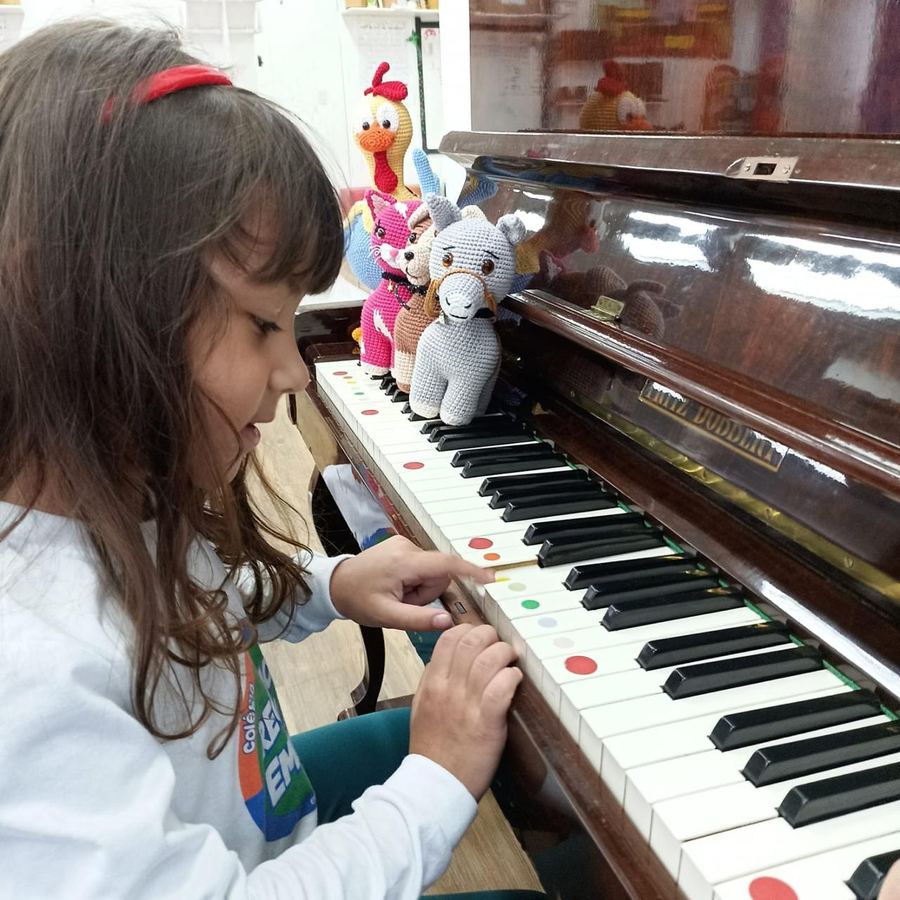 Menina de uniforme do colégio tocando piano, com bichinhos de pelúcia sobre o instrumento